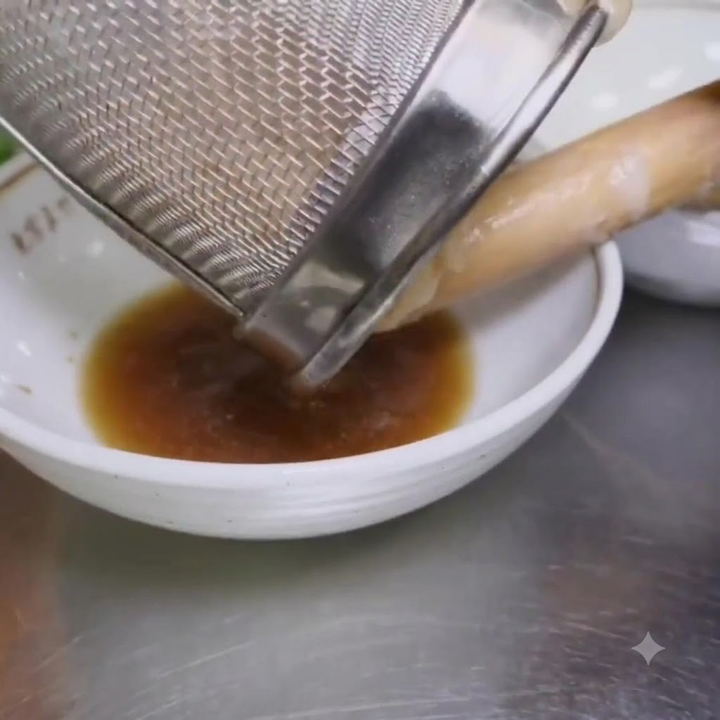 Noodles ramen bolliti versati da un colino a maglie in una ciotola contenente il condimento.