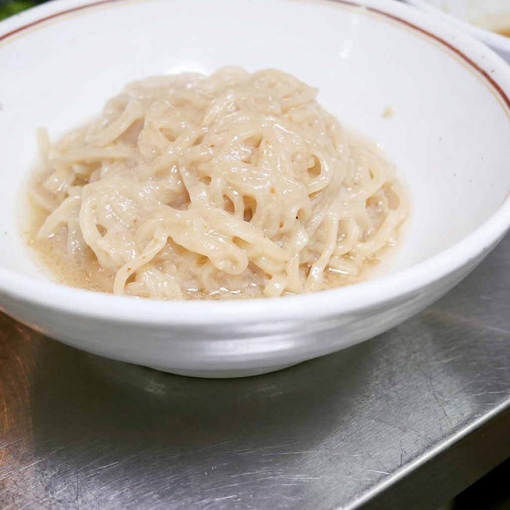 Noodles ramen cotti sistemati ordinatamente allinterno di una ciotola bianca, pronti per essere mescolati con la salsa.