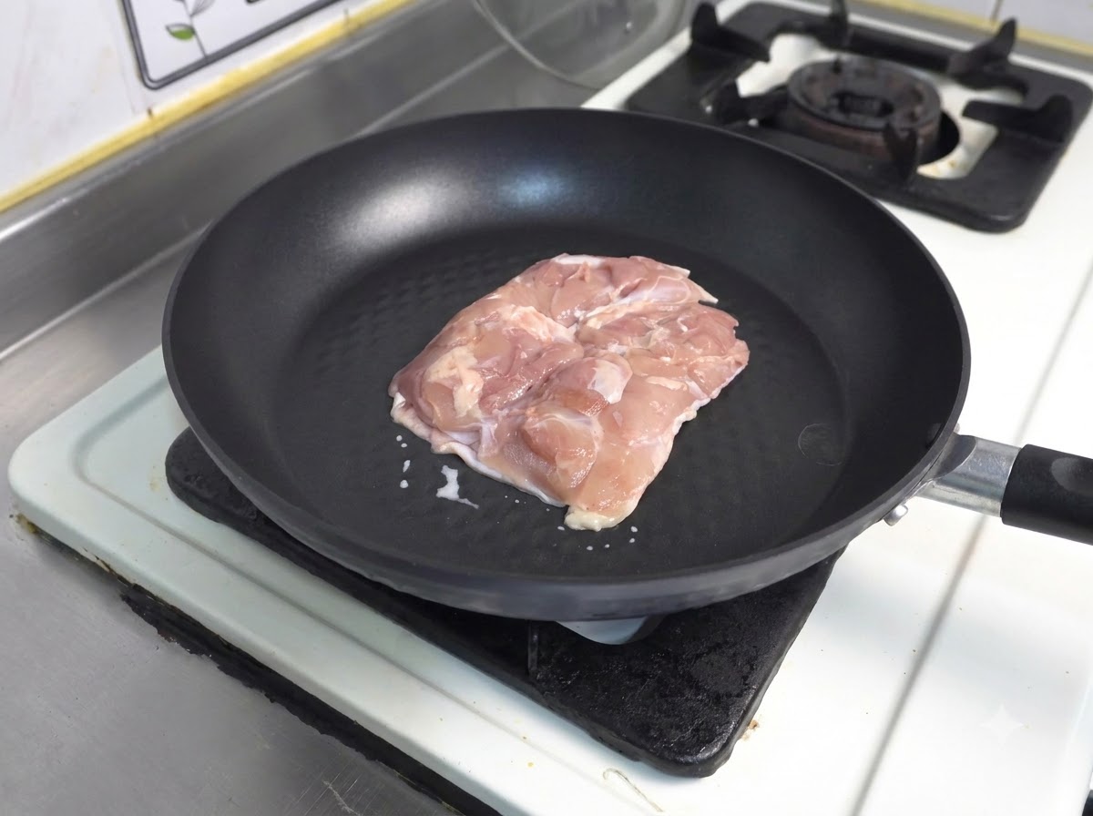 Un pezzo di coscia di pollo cruda con la pelle rivolta verso il basso in una padella antiaderente scura.