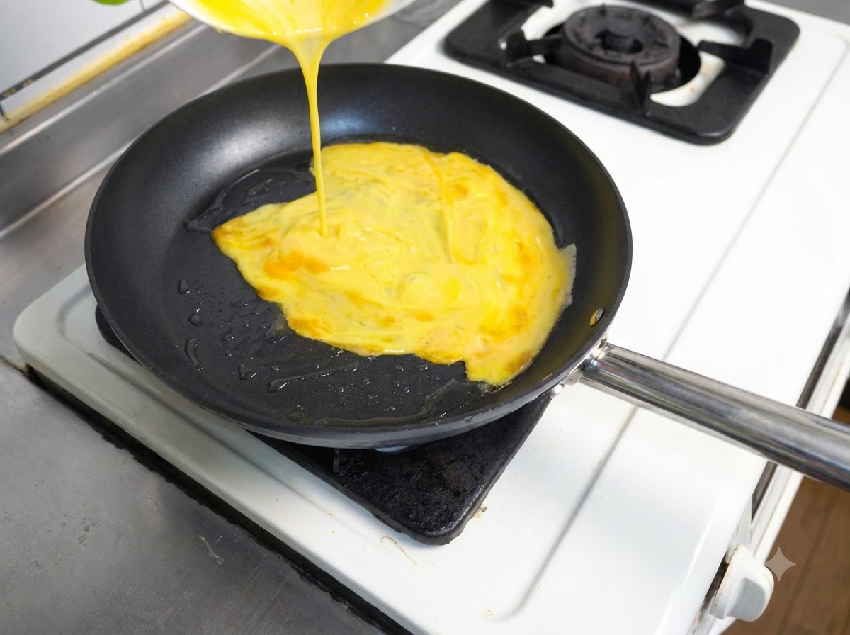 Uova gialle sbattute versate da un contenitore in una padella calda contenente olio.