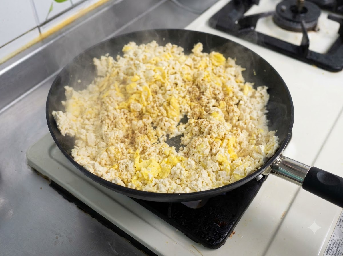 Una padella piena di una miscela di uova strapazzate e tofu fatta saltare con condimento cosparso sopra.