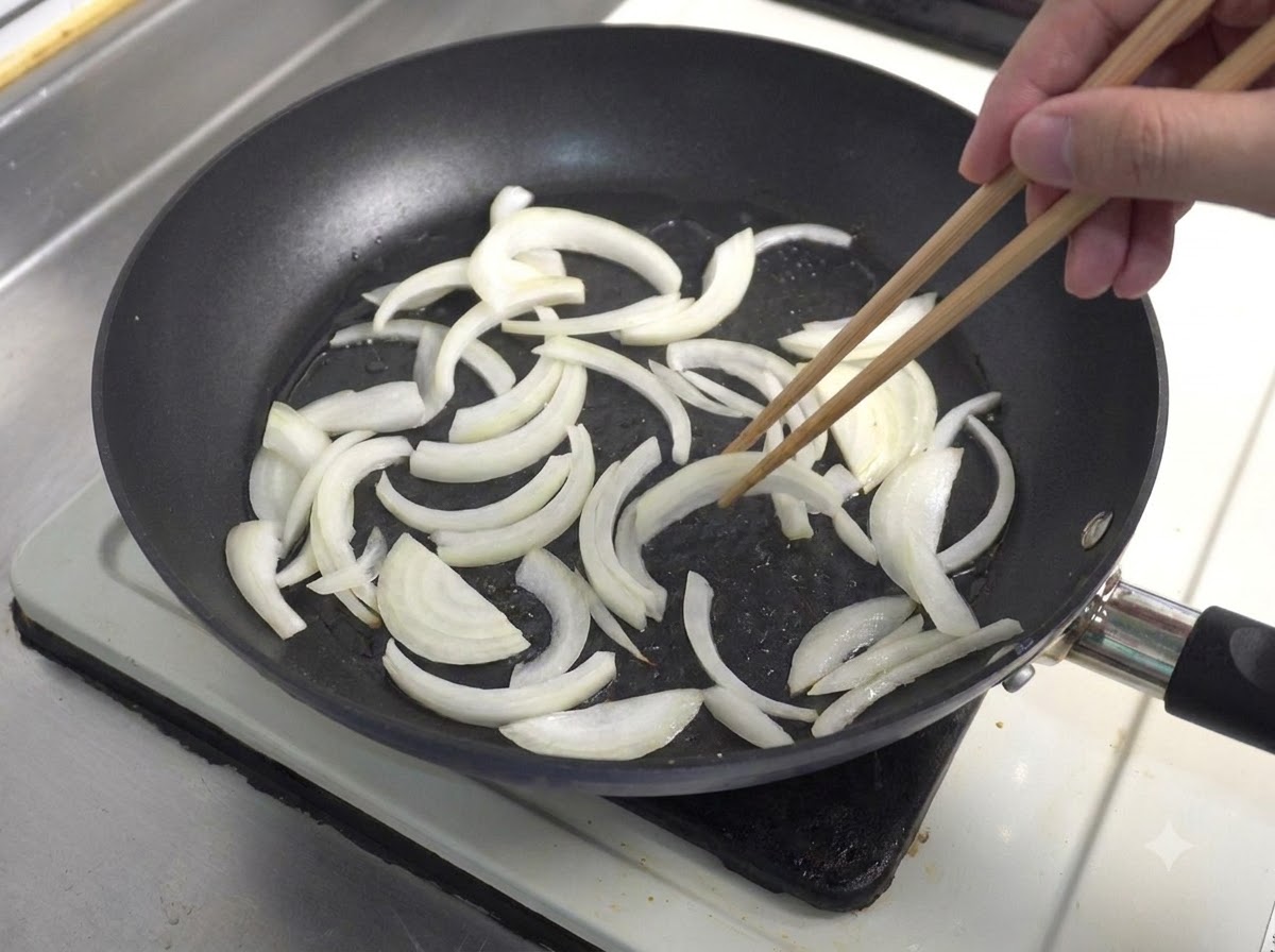 Cipolle bianche affettate saltate in padella con bacchette di legno.