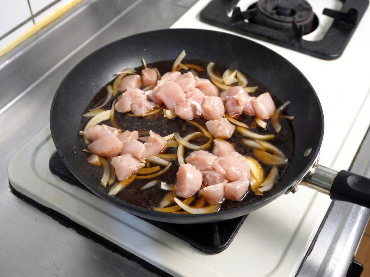 Pezzi di pollo crudo messi in una salsa scura e fumante con cipolle allinterno di una padella.