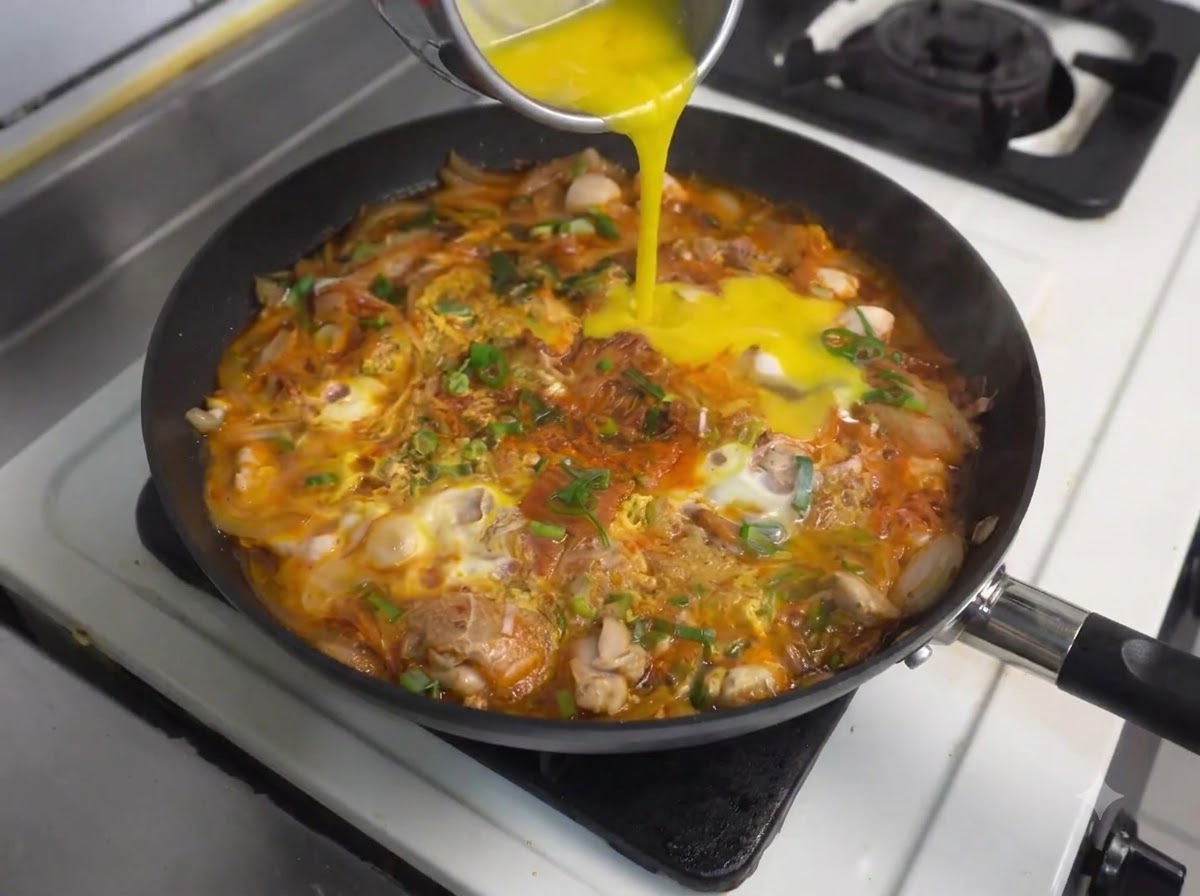 Versare altre uova sbattute da un contenitore nella padella in ebollizione con pollo e kimchi.