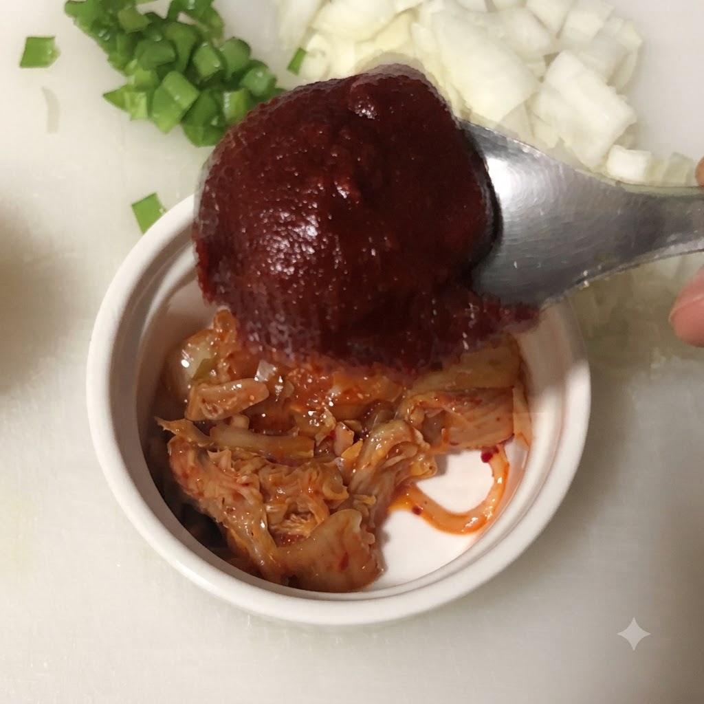 Un cucchiaio di pasta di peperoncino coreano tenuto sopra una ciotola contenente kimchi tritato.