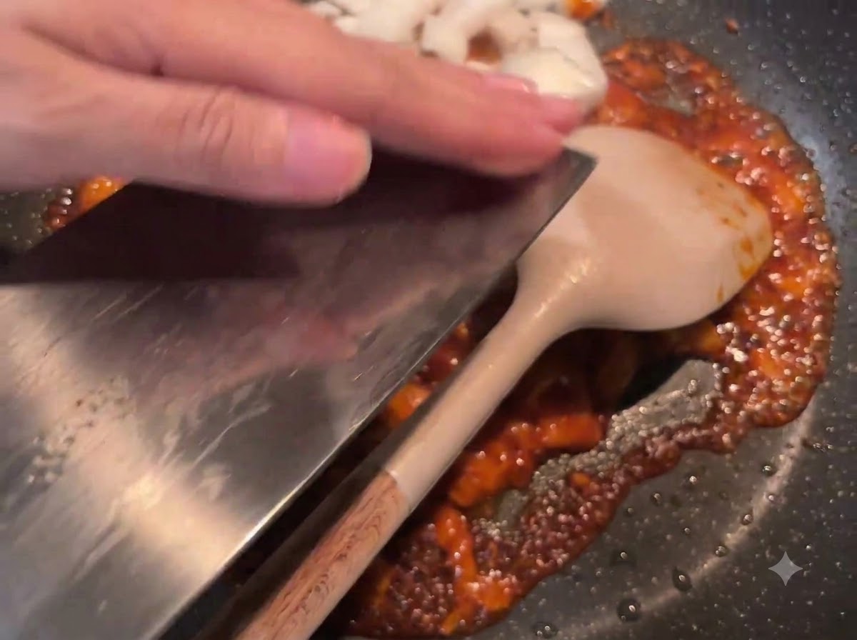 Cipolle bianche tagliate a cubetti raschiate da una mannaia nella padella contenente la salsa rossa saltata.