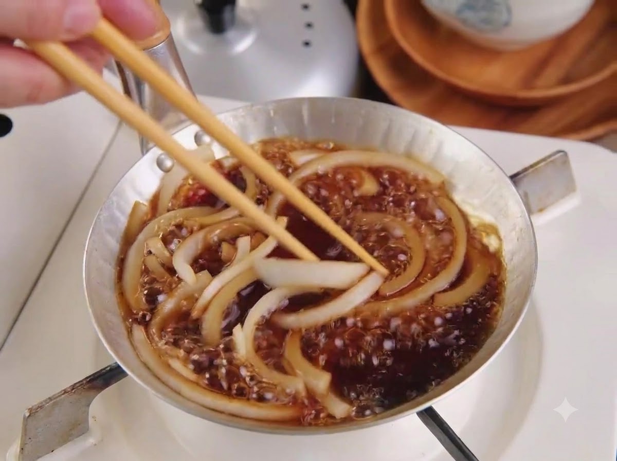 Una cotoletta di maiale affettata posizionata in una padella sopra cipolle e salsa in ebollizione usando le bacchette di legno.