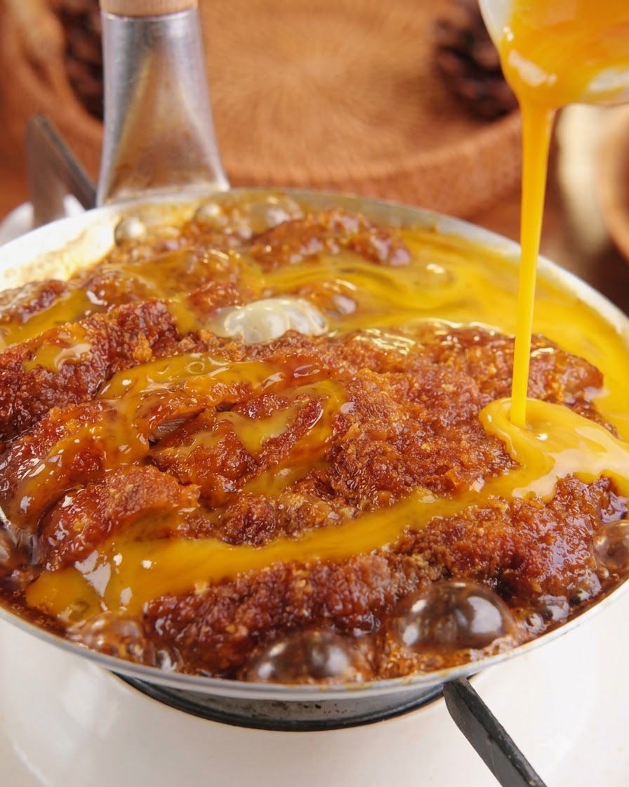 Composto di uovo giallo sbattuto versato dallalto sulla cotoletta di maiale in ebollizione dentro una padella.