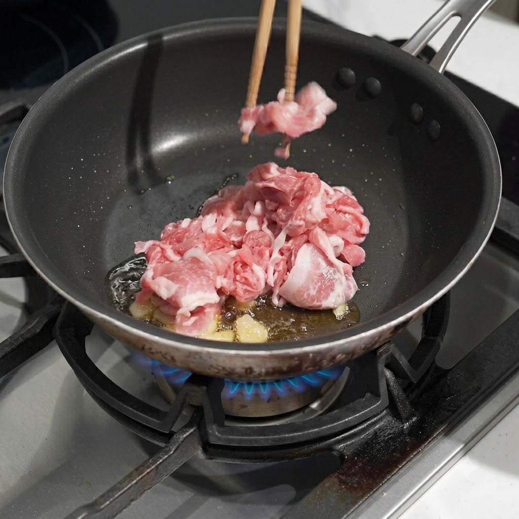 Maiale crudo tagliato sottile aggiunto in una padella con olio caldo e aglio mentre viene mescolato con le bacchette.