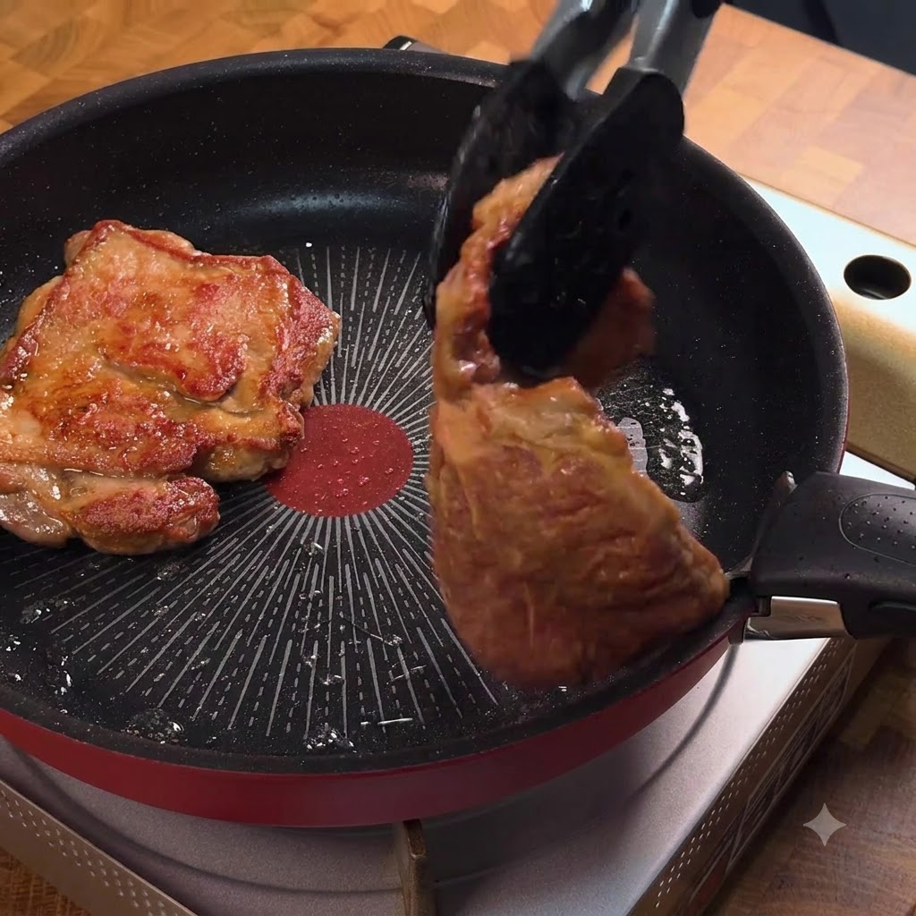 Pinze che girano una cotoletta di maiale dorata in una padella.