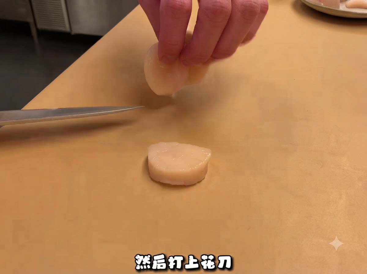 Un coltello da chef appoggiato vicino a una capasanta cruda affettata su un tagliere, con le mani che maneggiano un pezzo sopra.