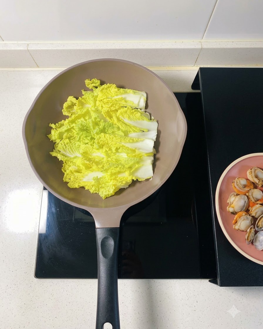 Noodle vermicelli inzuppati stratificati direttamente sopra il cavolo napa nella padella.