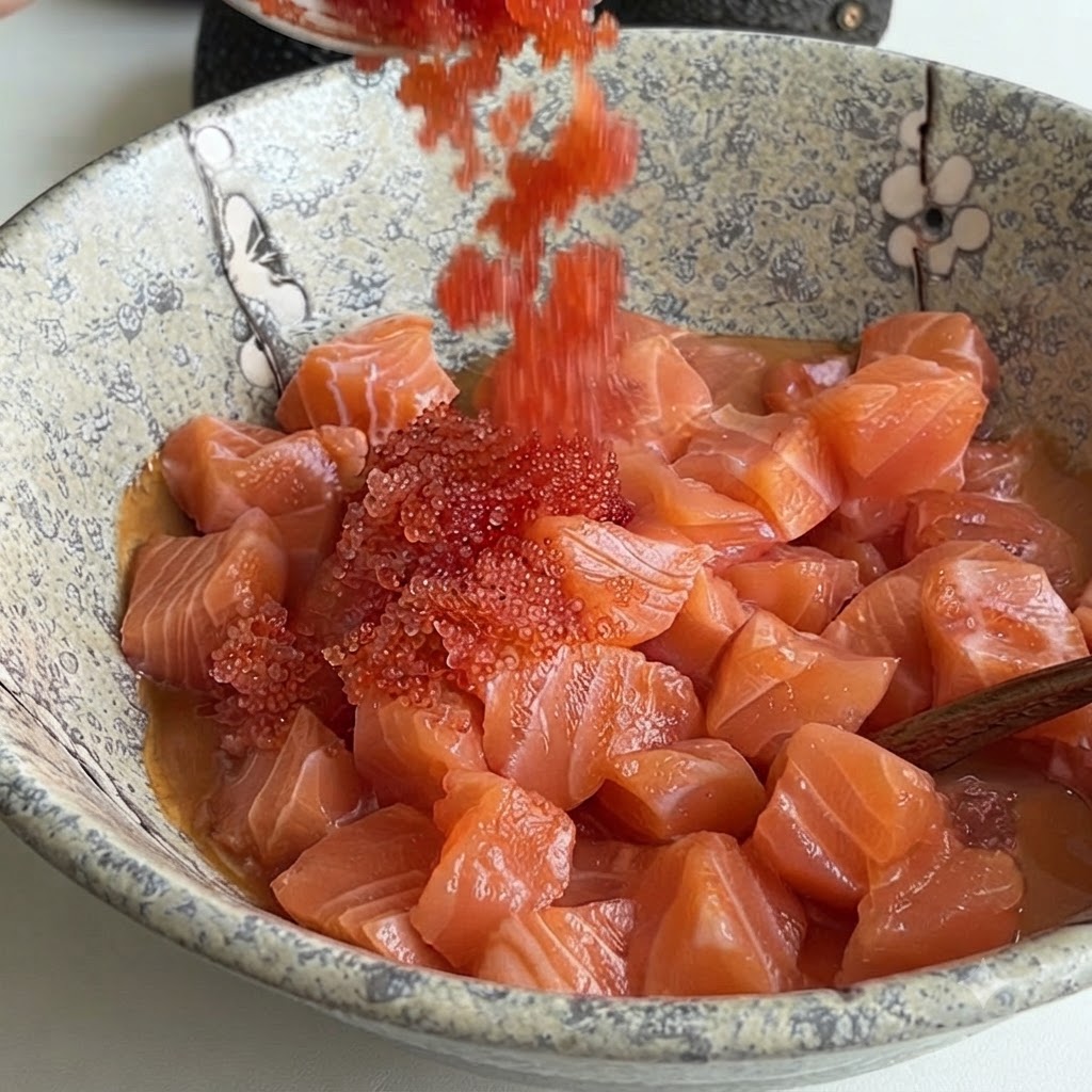Uova di pesce rosso brillante versate da un cucchiaio in una ciotola di ceramica piena di salmone a dadini e salsa.
