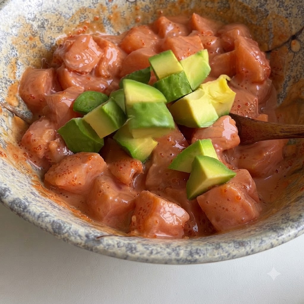 Cubetti di avocado verde delicatamente incorporati in una ciotola di cubetti di salmone ricoperti da una salsa rosa cremosa.