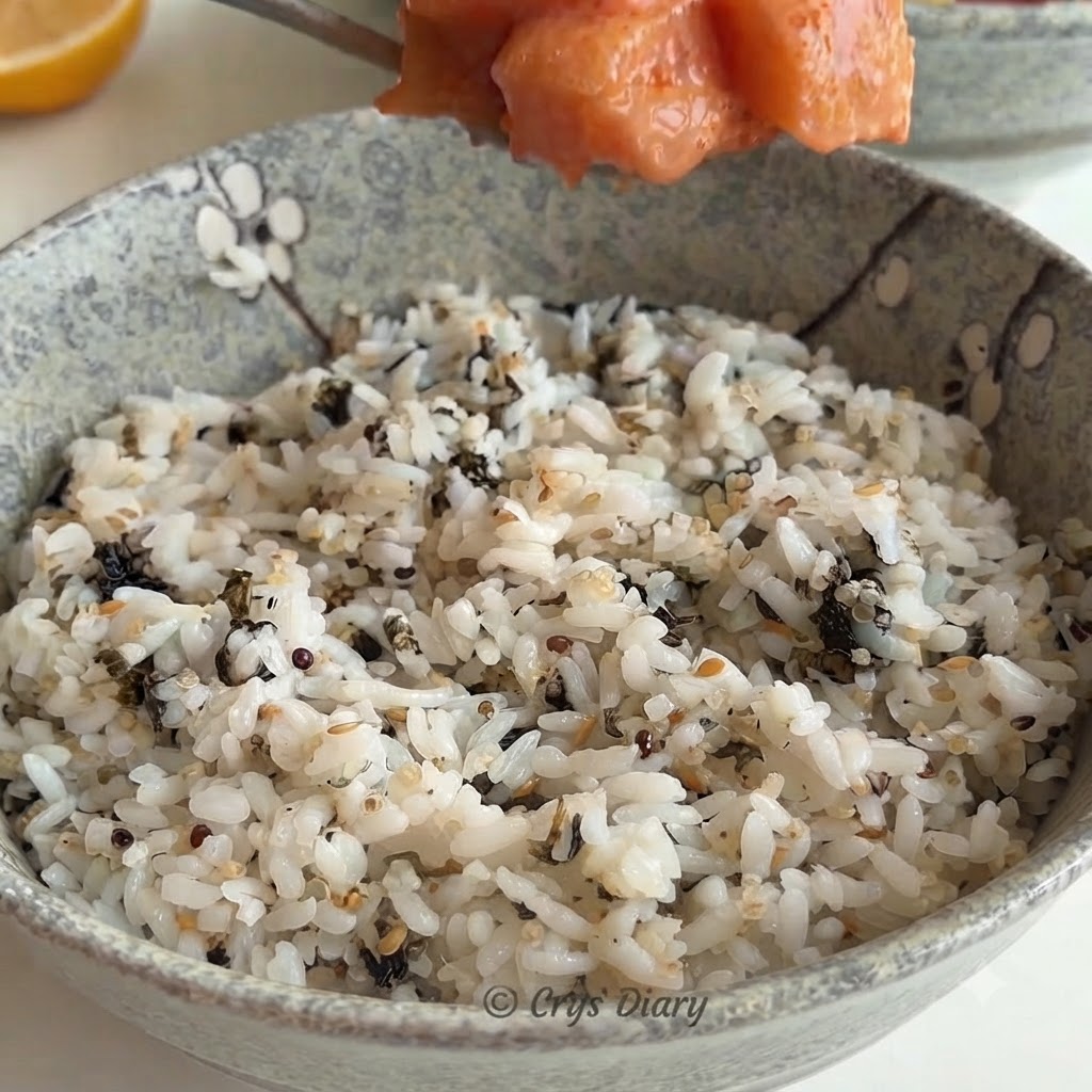 Un cucchiaio di composto di salmone posizionato sopra una ciotola di ceramica piena di riso bianco e scaglie di alga.