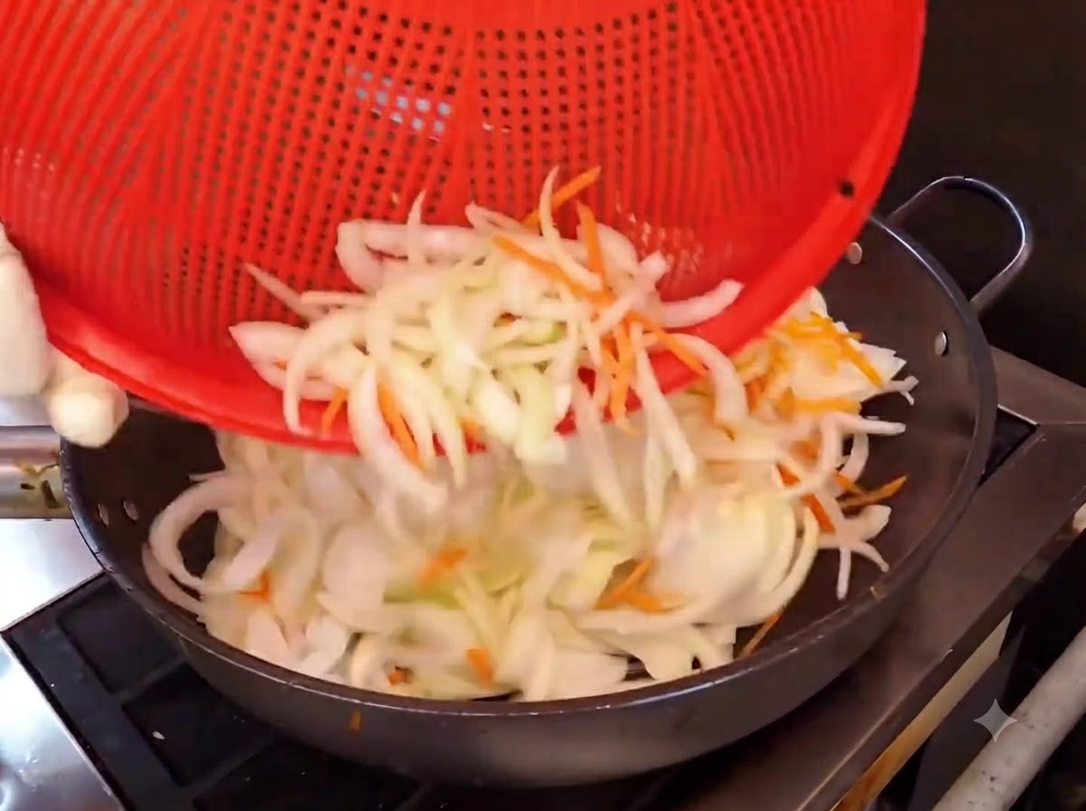 Strisce di cipolla e carota versate da un cestino rosso in un wok caldo per la cottura.