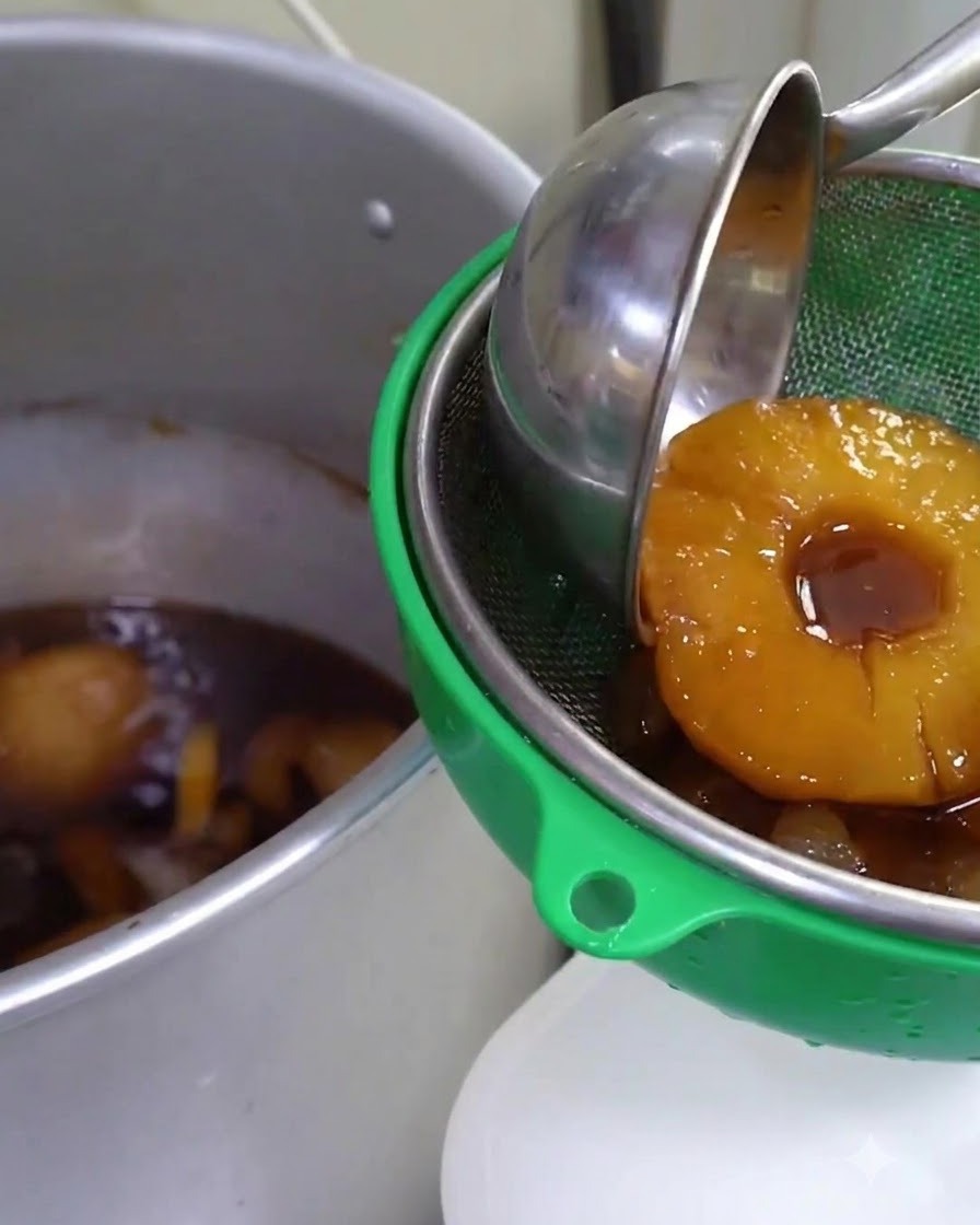 Salsa aromatizzata alla frutta fatta sobbollire filtrata attraverso un setaccio verde in un grande contenitore di metallo.