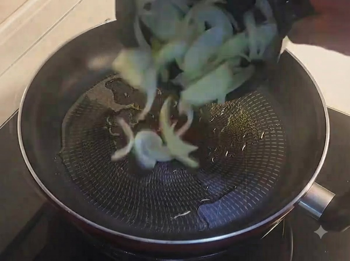 Cipolle dorate a fette versate in una padella nera oliata.