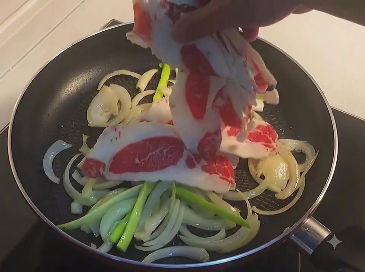 Una mano che mette sottili fette di pancetta di manzo cruda in una padella con cipolle e cipollotti affettati.