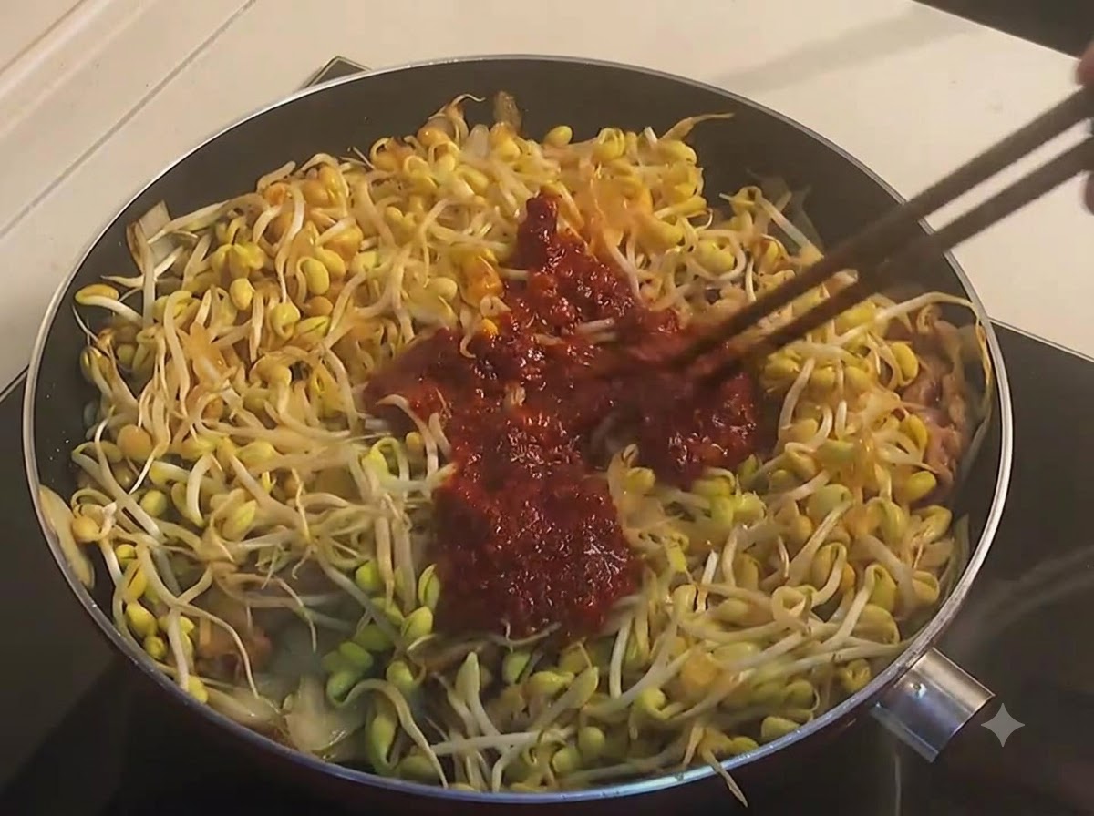 Bacchette che mescolano germogli di soia gialli e manzo con una densa salsa rossa piccante in una padella.
