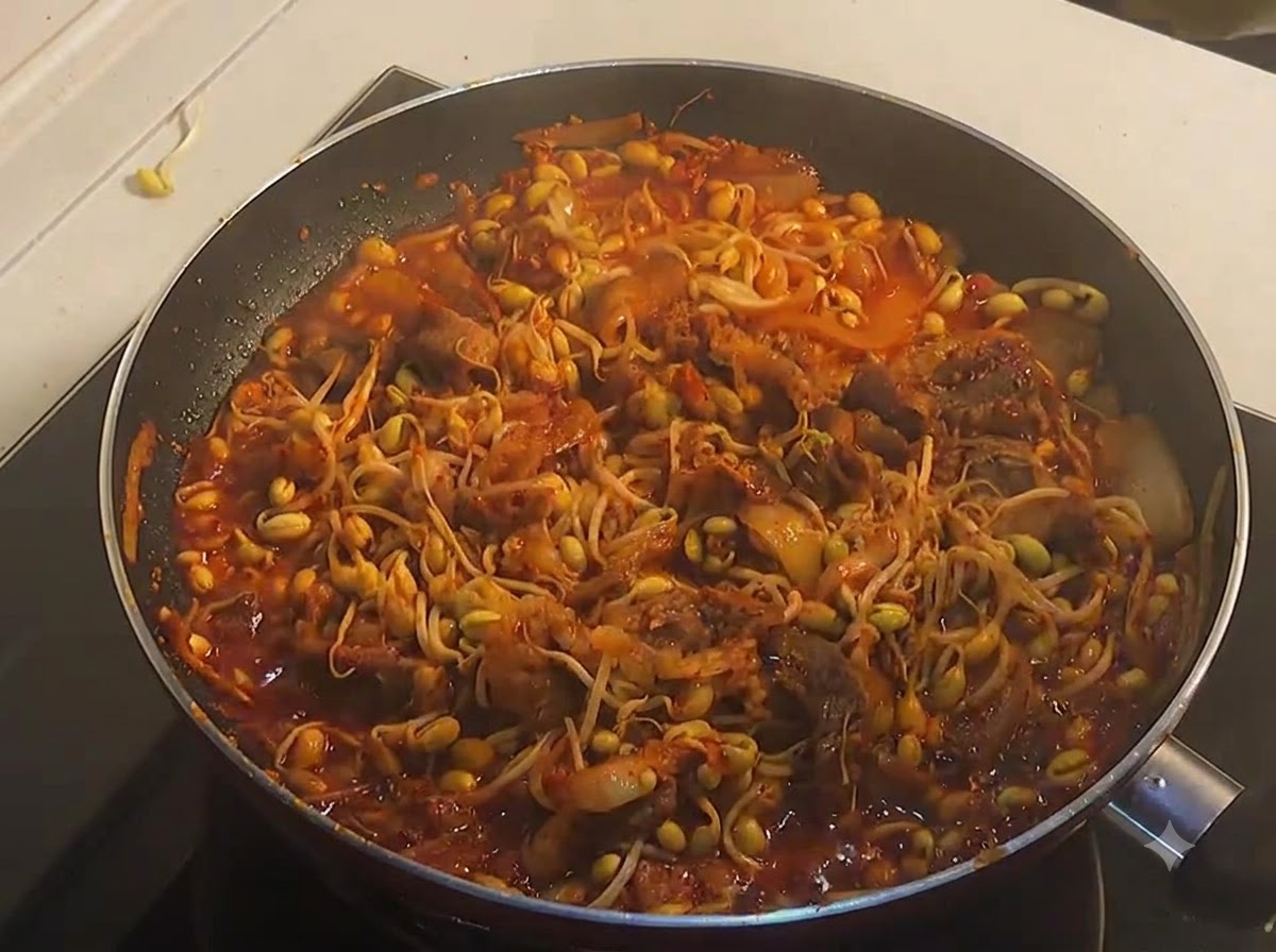 Una padella piena di manzo piccante e germogli di soia gialli ben cotti e fumanti in una ricca salsa rossa.
