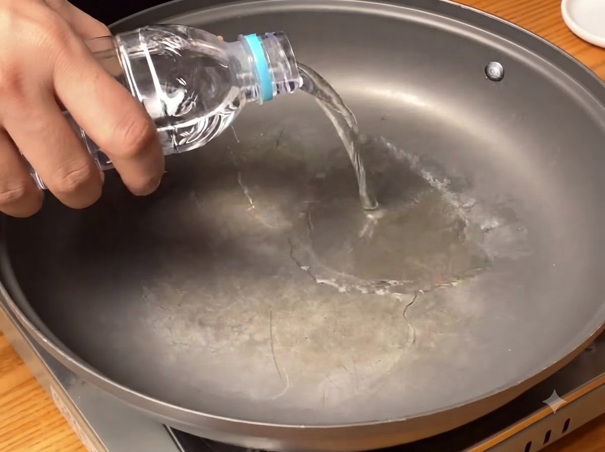 Acqua pulita versata da una bottiglia sul fondo di una padella larga.