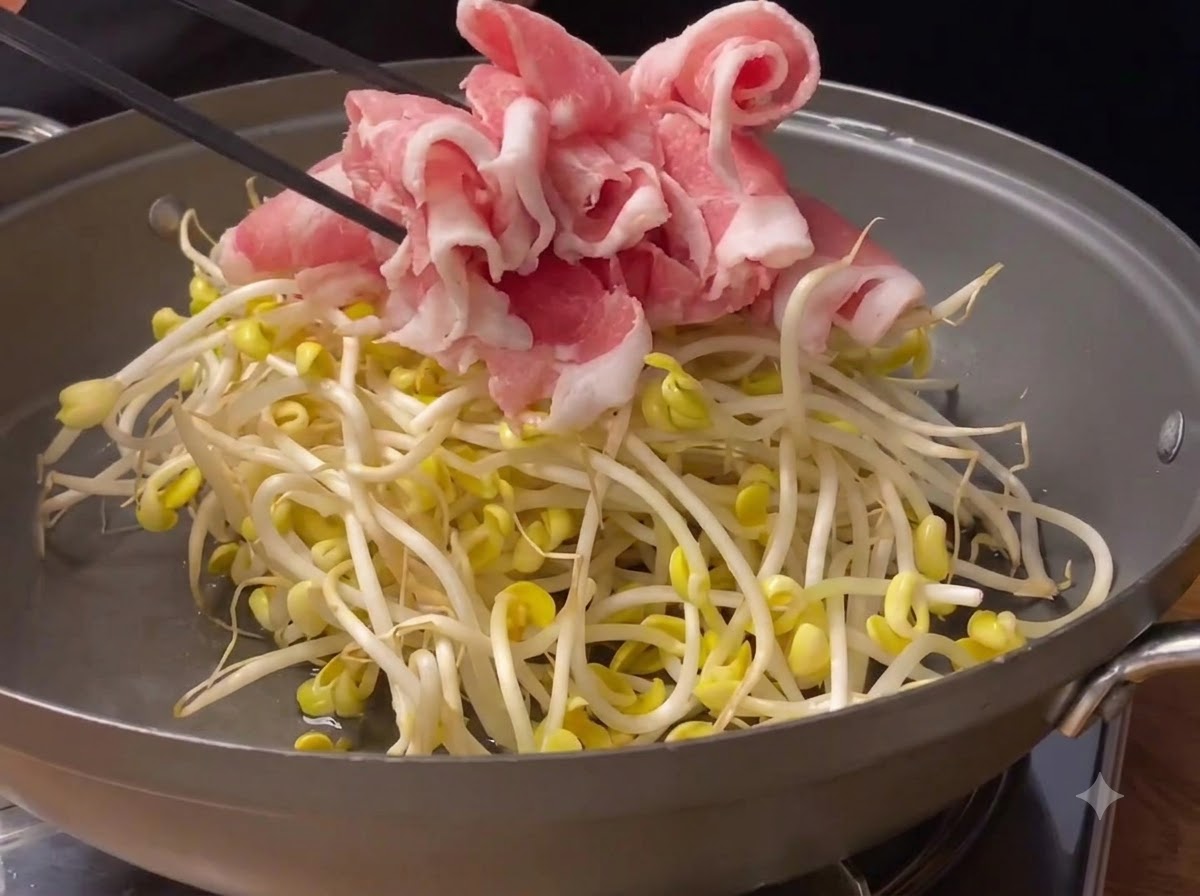 Involtini di maiale rosa affettati sottilmente posizionati sopra i germogli di soia freschi allinterno di una padella.