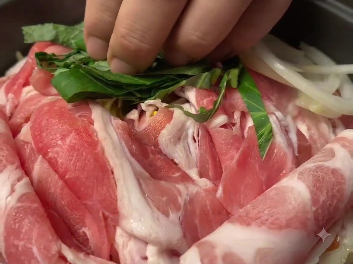 Foglie di perilla verde tagliate sparse sopra le fette di maiale crudo nella padella.