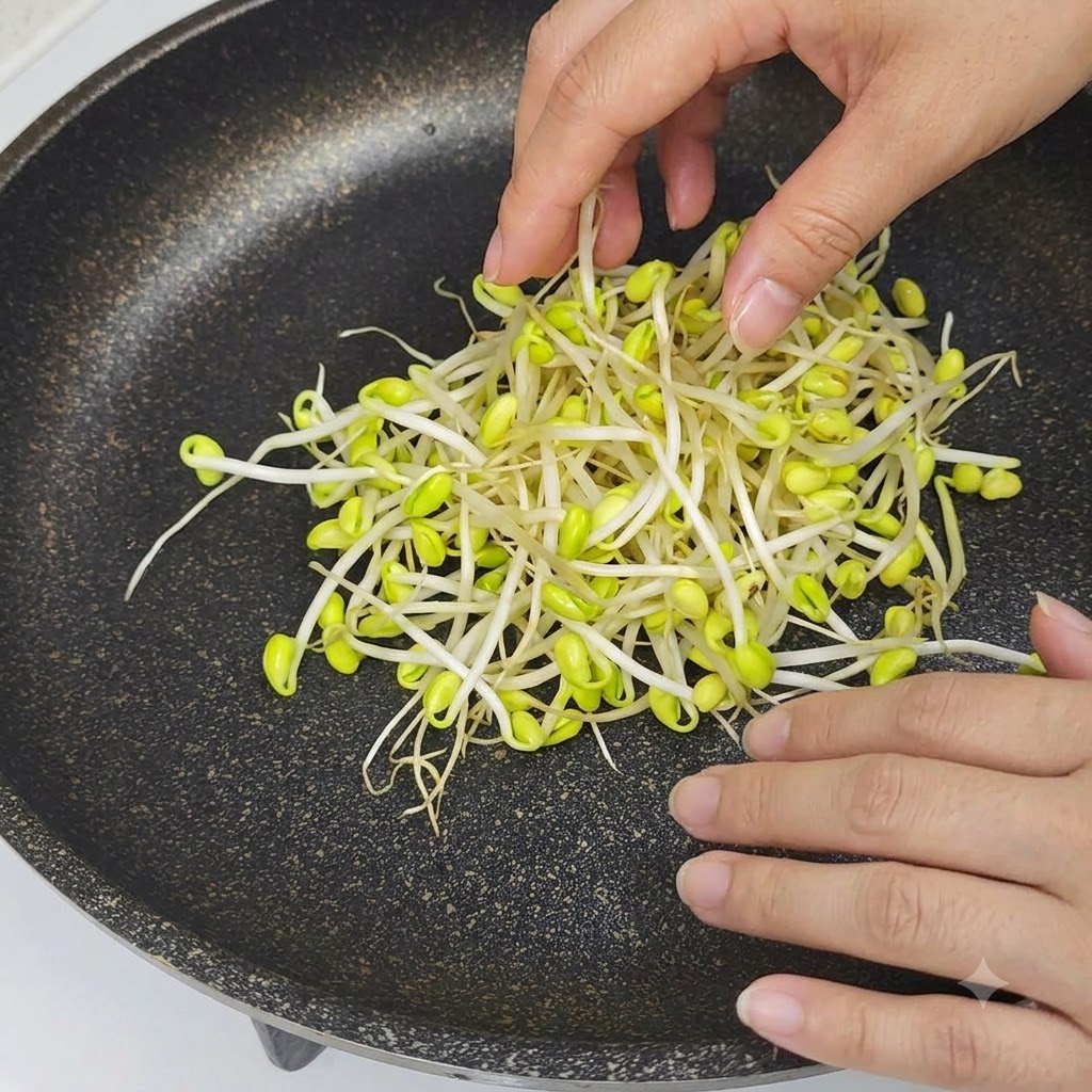 Mani che posizionano germogli di soia crudi con le punte gialle al centro di una padella antiaderente nera.