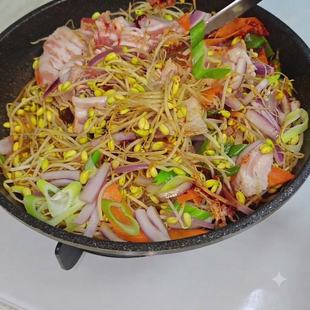 Un utensile da cucina che mescola i germogli di soia misti, la pancetta di maiale e le verdure allinterno di una padella sul fuoco.