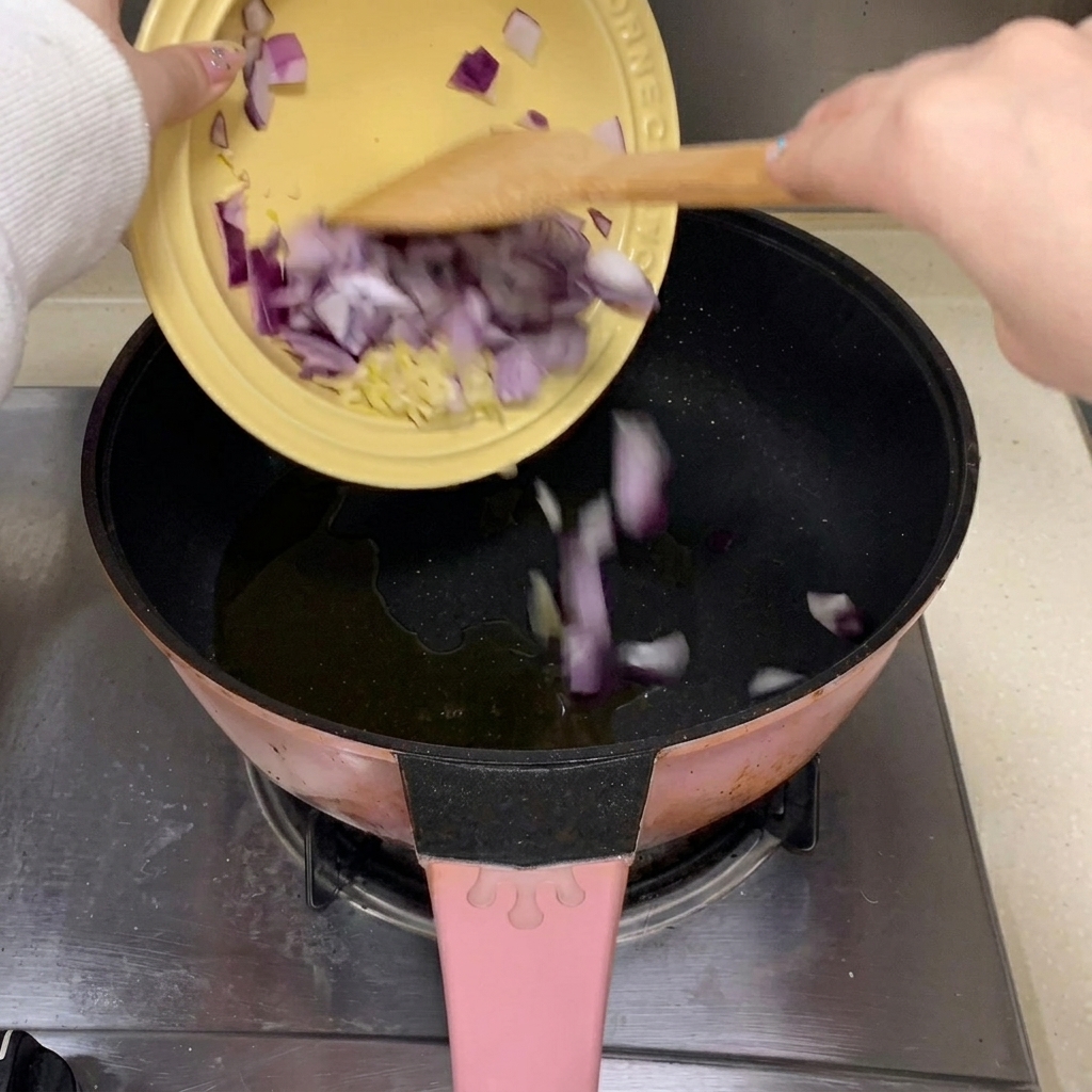 Pezzi di aglio tritato e cipolla rossa che cadono in una padella con olio da cucina caldo.
