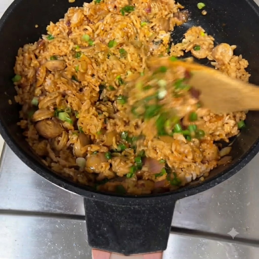 Riso saltato mescolato con una spatola di legno in una padella, guarnito con cipollotti.