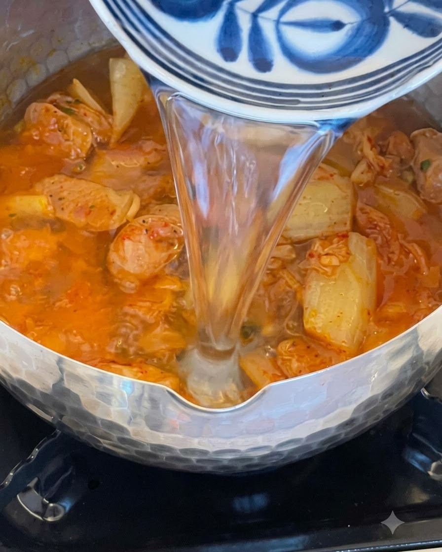 Acqua versata in una pentola piena di brodo rosso, kimchi e salsiccia in ebollizione.