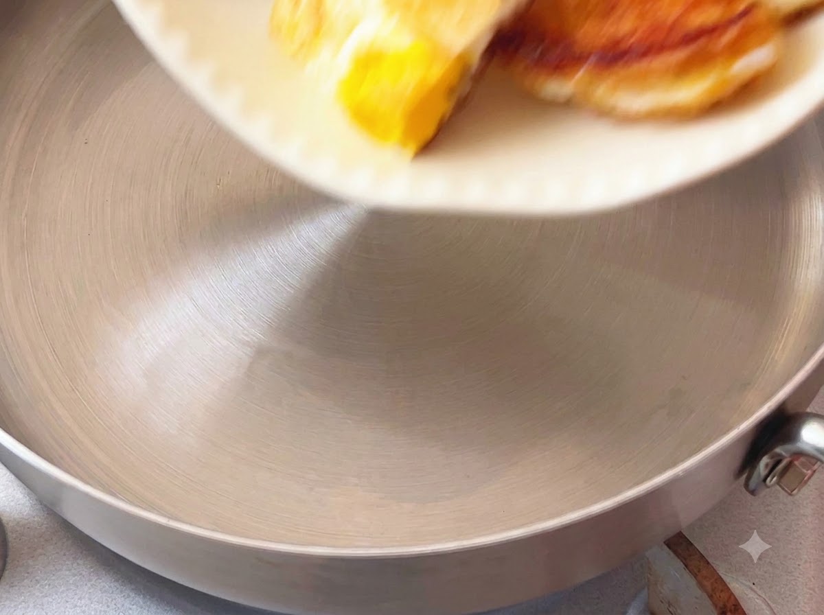Pezzi di uovo fritto fatti cadere in una pentola da cucina da un piatto bianco.