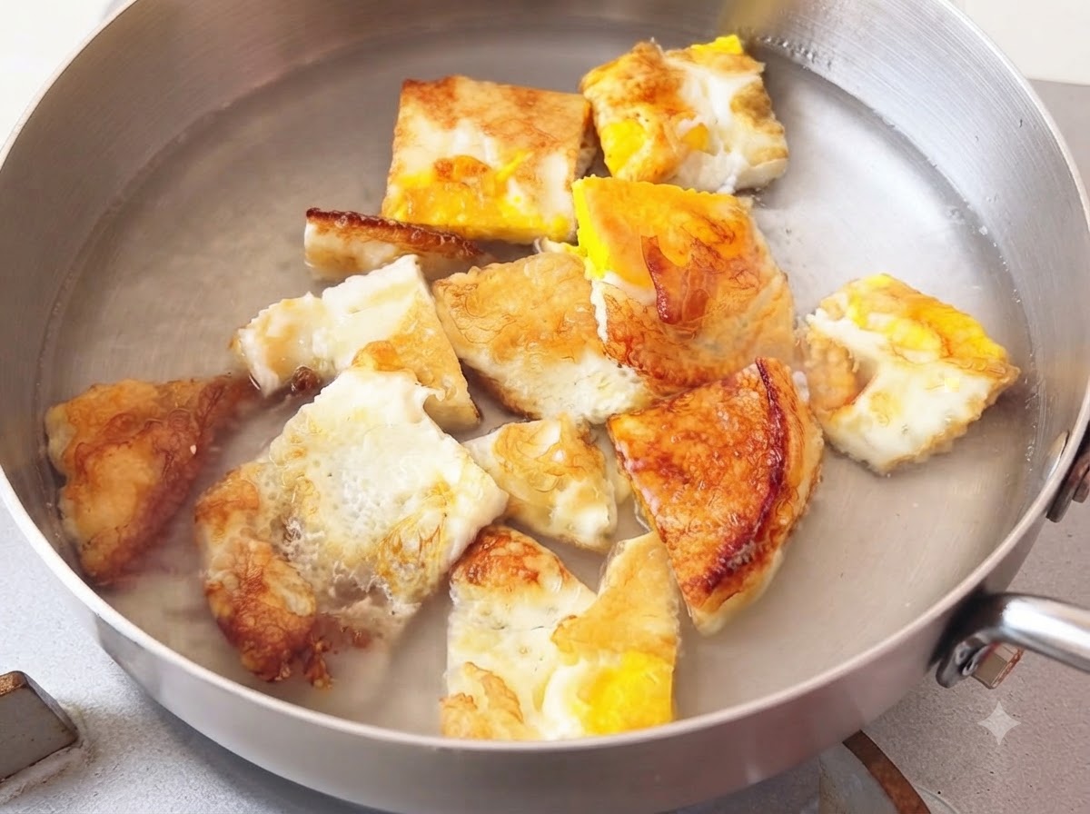 Acqua calda versata in una pentola di metallo contenente pezzi di uovo fritto.