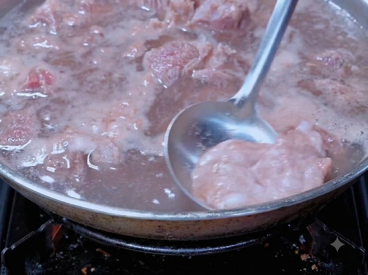 Un mestolo che rimuove la schiuma di sangue dal manzo in ebollizione in una pentola da cucina.
