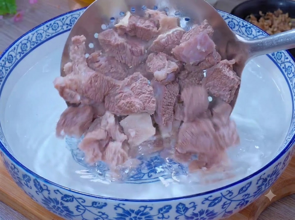 Pezzi di manzo sbollentati puliti allinterno di una ciotola di acqua tiepida usando un cucchiaio forato.