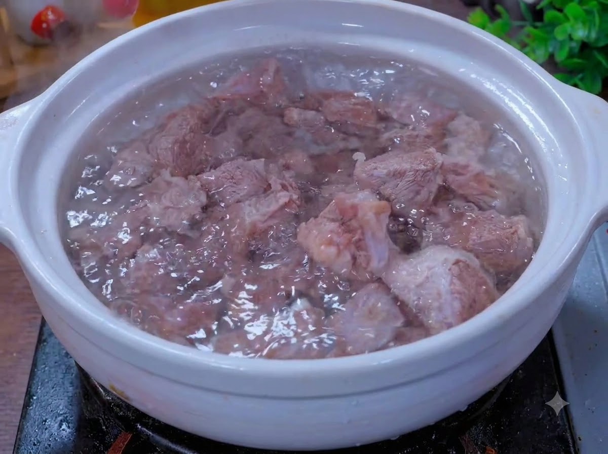 Pezzi di manzo che cuociono a fuoco lento in una pentola di coccio bianca con aromi.