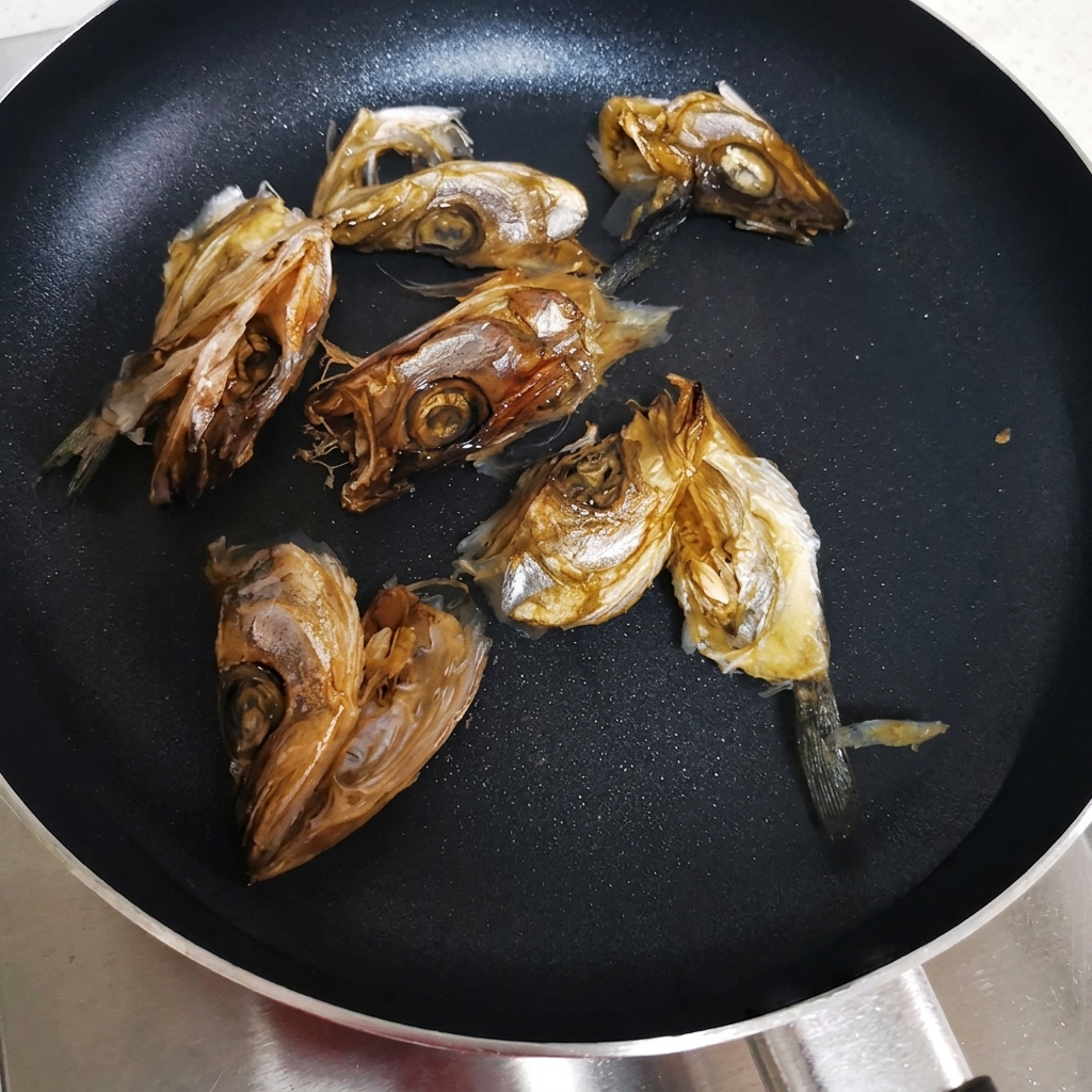 Teste di pesce essiccato disposte in una pentola larga con acqua fredda, pronte per essere scaldate.