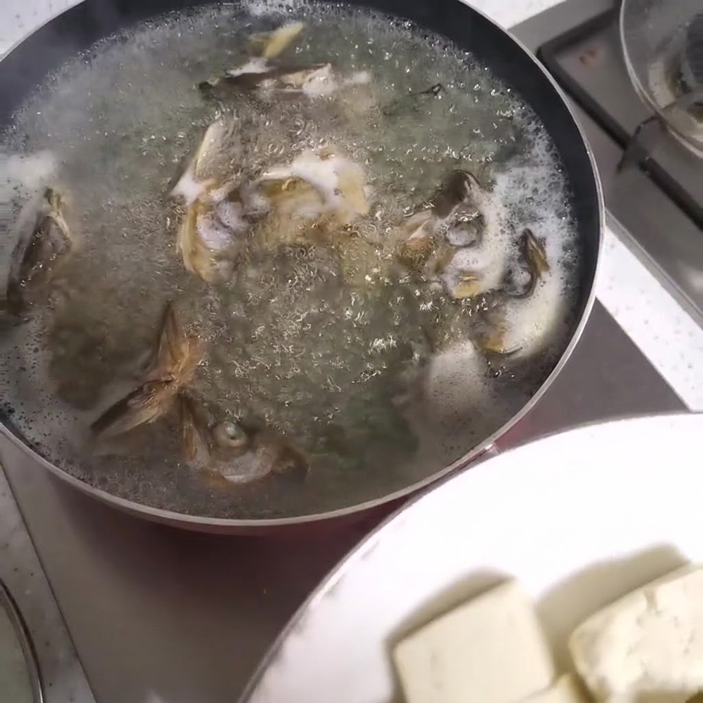 Cubetti di tofu aggiunti a una pentola fumante di zuppa di teste di pesce.