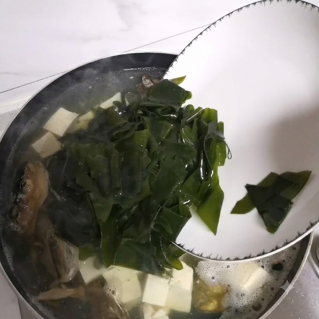 Pezzi di alga che scivolano da un piatto nella pentola della zuppa a fuoco lento.