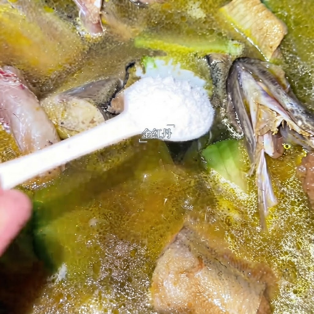 Un cucchiaio di condimento bianco aggiunto nella pentola di zuppa di merluzzo in ebollizione.