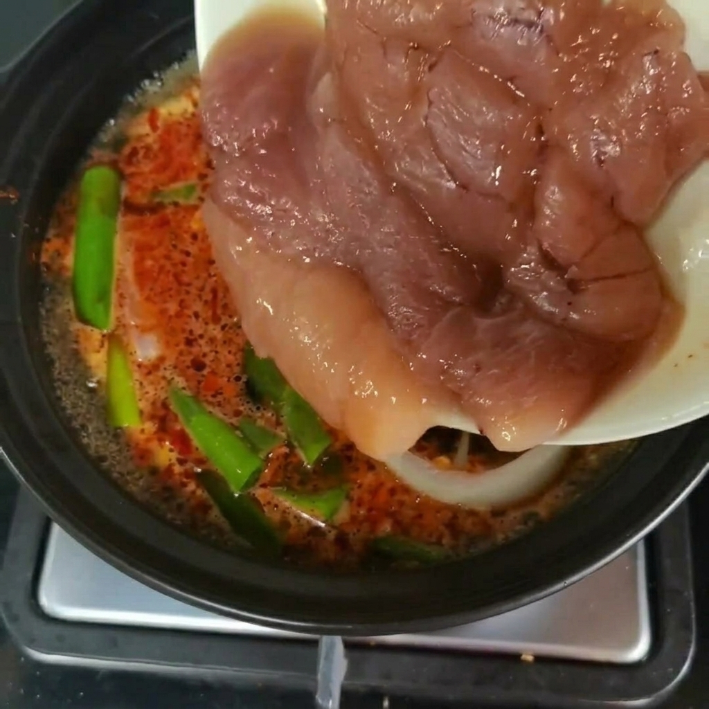 Freschi pezzi di uova di merluzzo trasferiti da un piatto in una pentola di zuppa in ebollizione con verdure verdi.