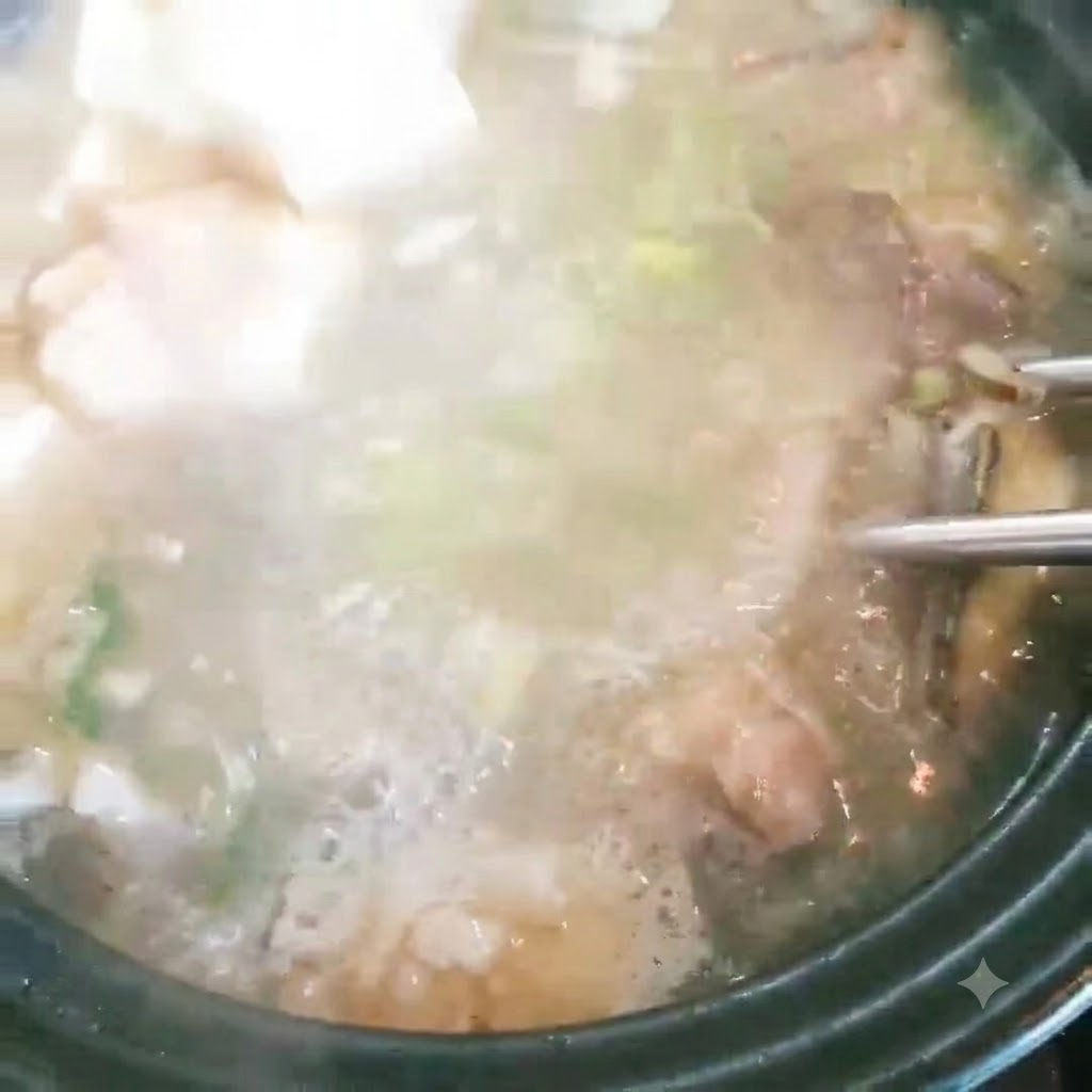Cubetti di tofu aggiunti a una pentola di zuppa di pesce che bolle con cipollotti.