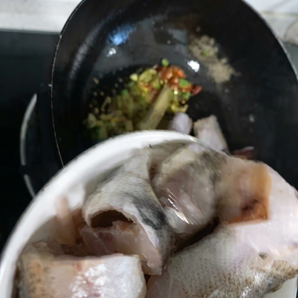 Pezzi di pesce merluzzo trasferiti da una ciotola nel wok.