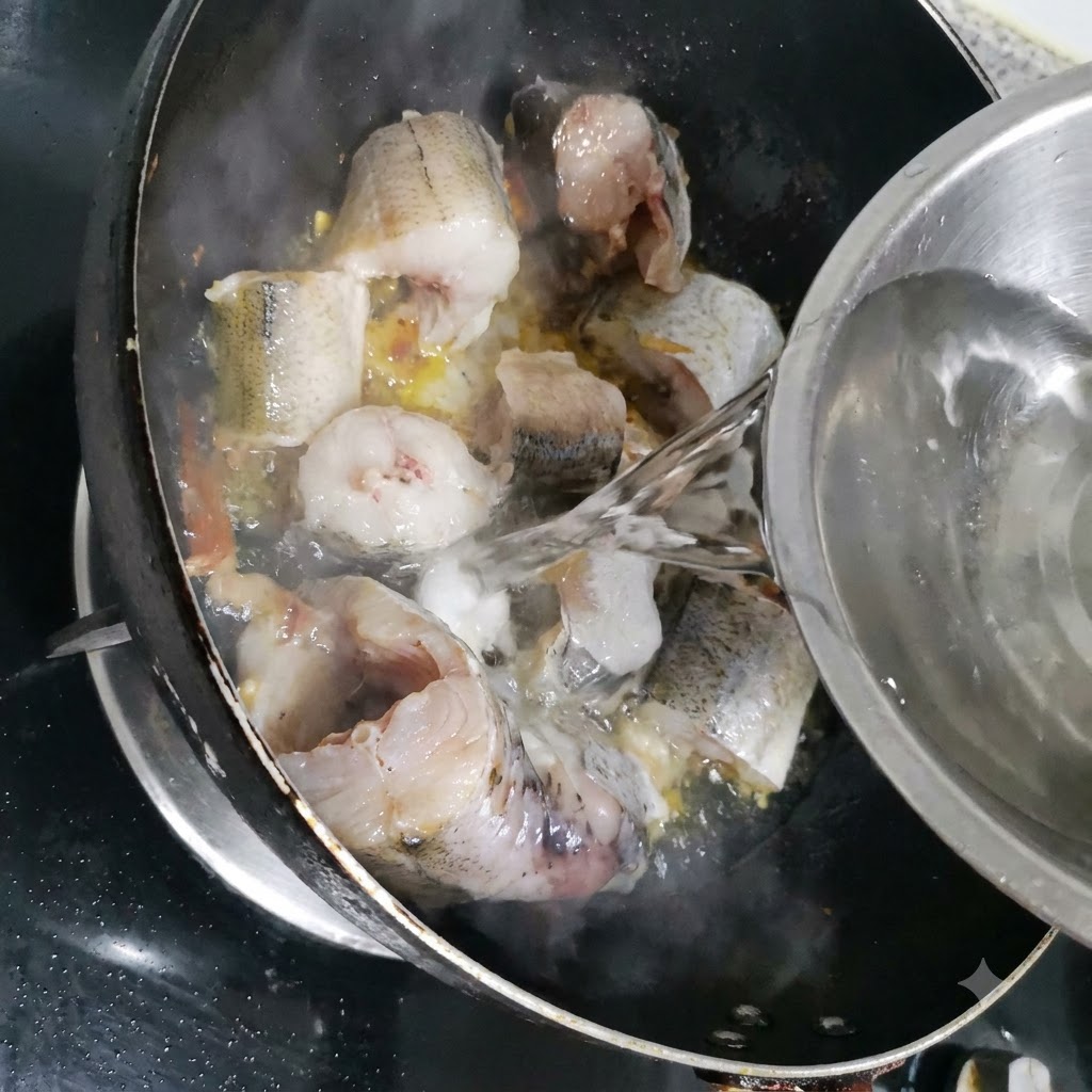 Acqua versata da una ciotola di metallo nella padella con i pezzi di merluzzo.