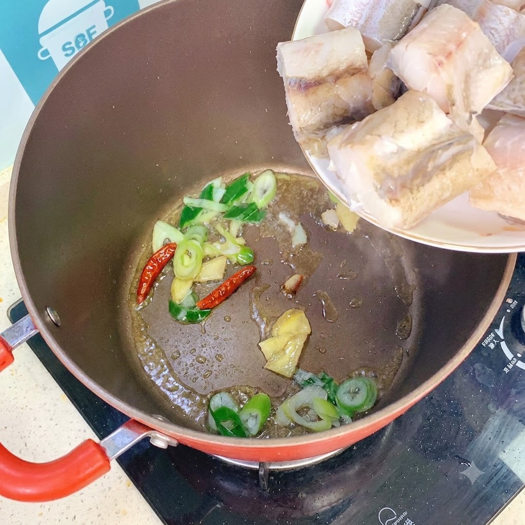 Pezzi di merluzzo aggiunti nella pentola con il soffritto di cipollotti, zenzero e peperoncini.