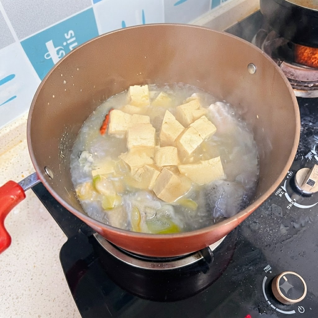Una pentola di zuppa di pesce e tofu che sobbolle sul fornello, con un brodo dal colore opalescente.