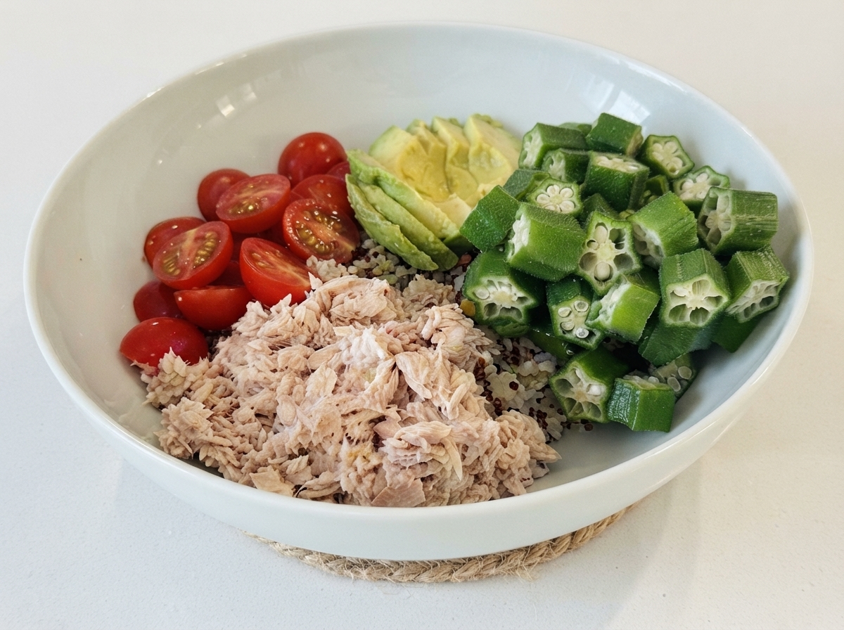 Una ciotola bianca riempita con una base di riso, sormontata da sezioni di tonno, pomodorini, avocado a fette e okra.