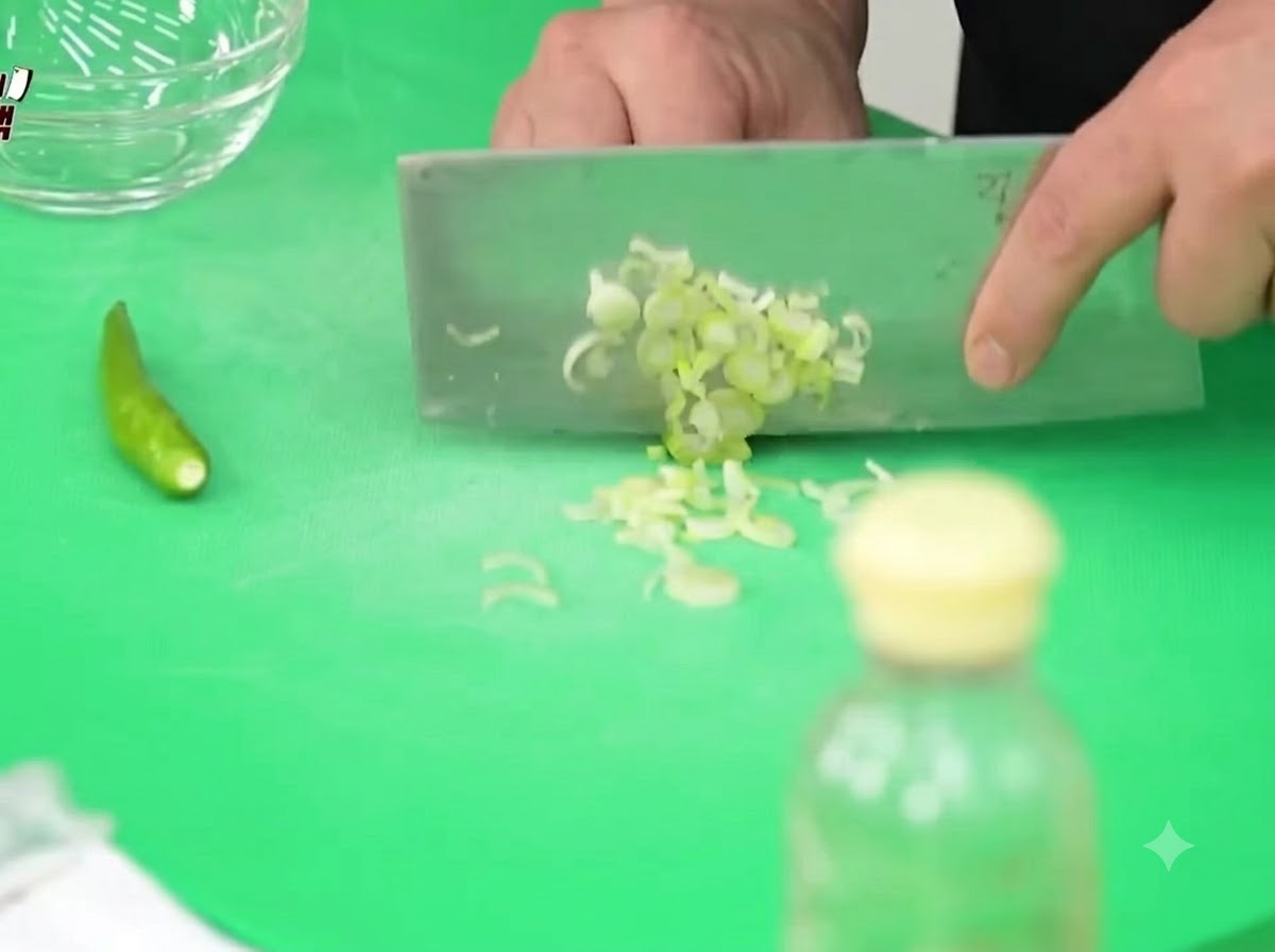 Cipollotti, peperoncini Cheongyang e cipolle tagliati finemente su un tagliere verde con una mannaia.